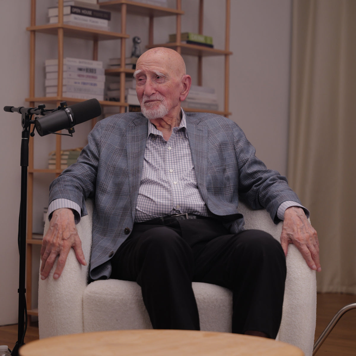 Dominic Chianese seated in a white armchair beside a studio microphone